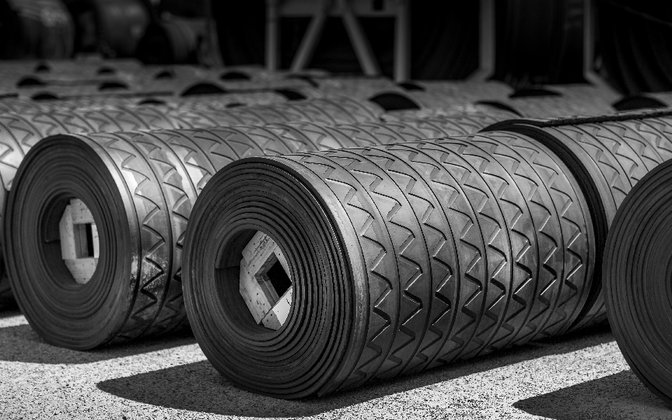 Heavy-duty rubber rolls with a zigzag grip tread lined up outdoors, EasyMat rubber flooring in roll form